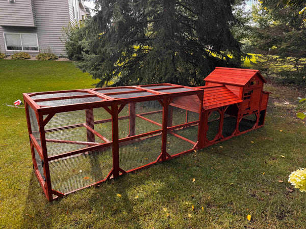 Leghorn Cottage Coop with run: elevated red wooden hen house, nesting spaces, wire-enclosed run, predator-resistant design in a lawn.