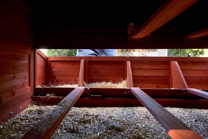 Internal view of a large red chicken coop with wooden roosting bars and three separate nesting compartments.