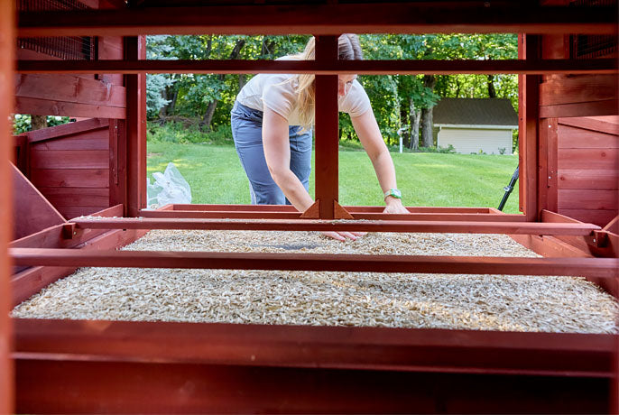 Internal view of a red chicken coop with a deep pull-out cleaning tray and wooden roosting bars for flock comfort.