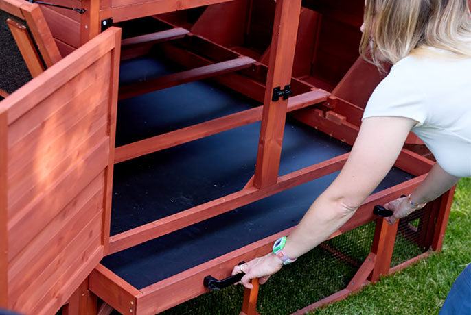Large pull-out metal cleaning tray with black handles for easy maintenance of a red wooden chicken coop.
