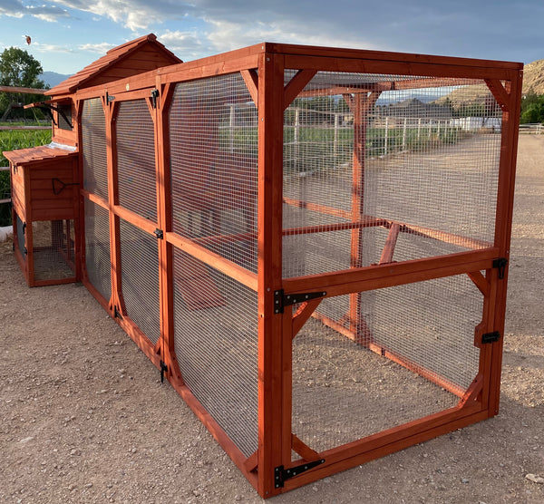 A red wooden chicken coop chickens set outdoors with a partly cloudy sky in the background.