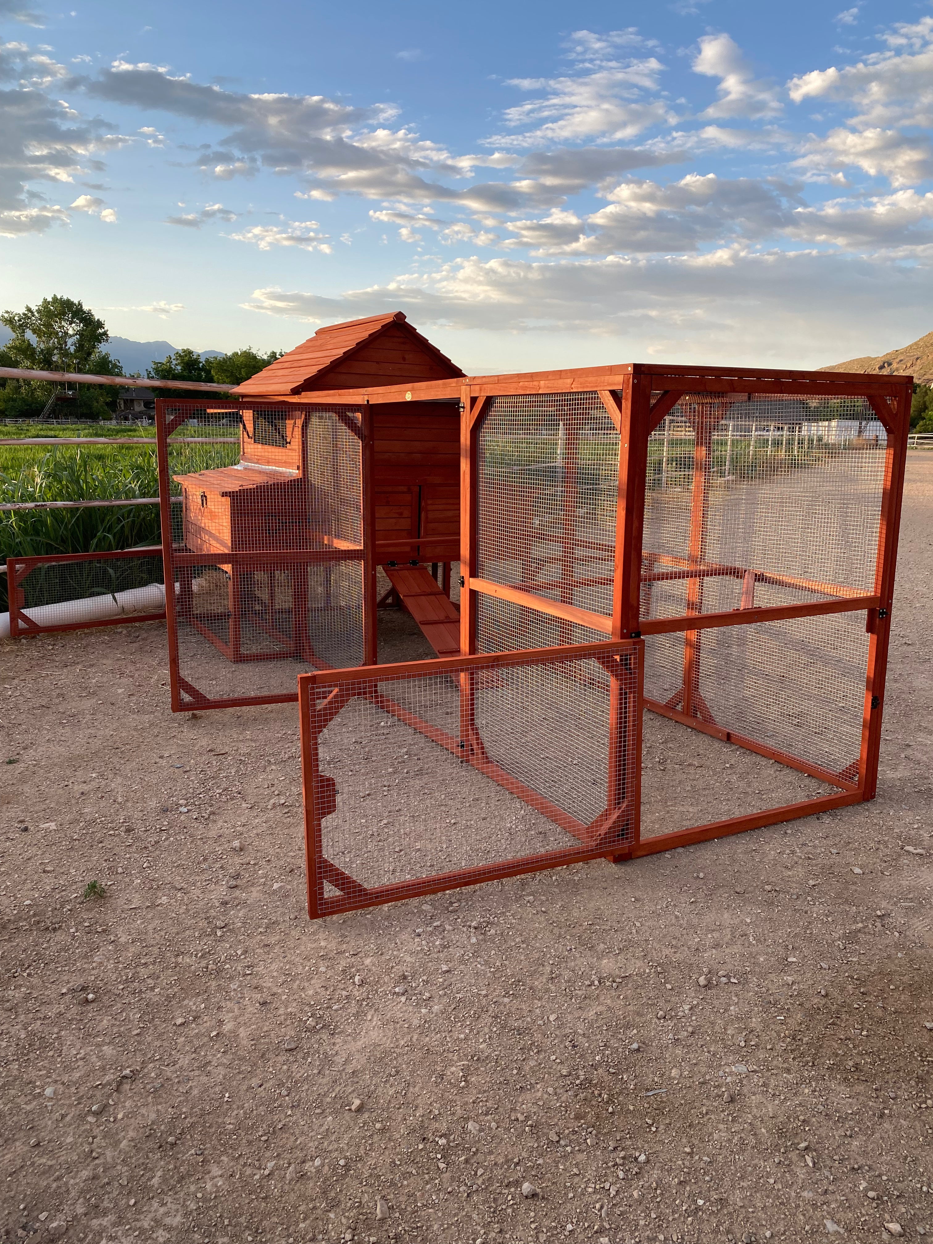 A red wooden chicken coop for  chickens set outdoors with a partly cloudy sky in the background.