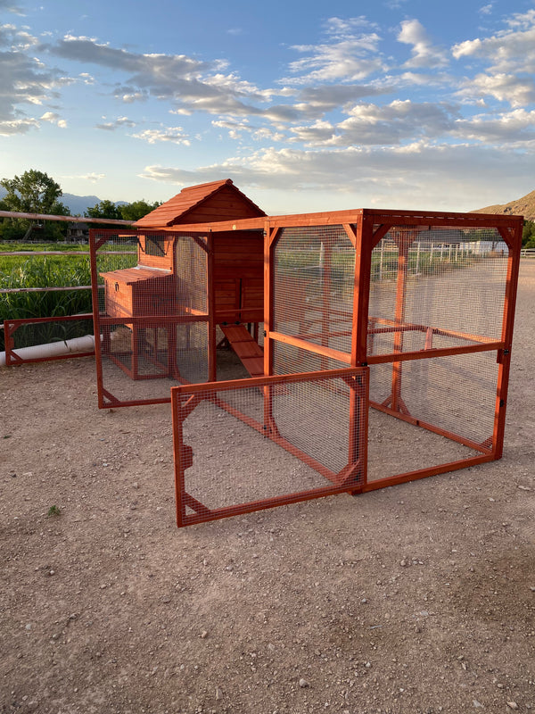 A red wooden chicken coop for  chickens set outdoors with a partly cloudy sky in the background.